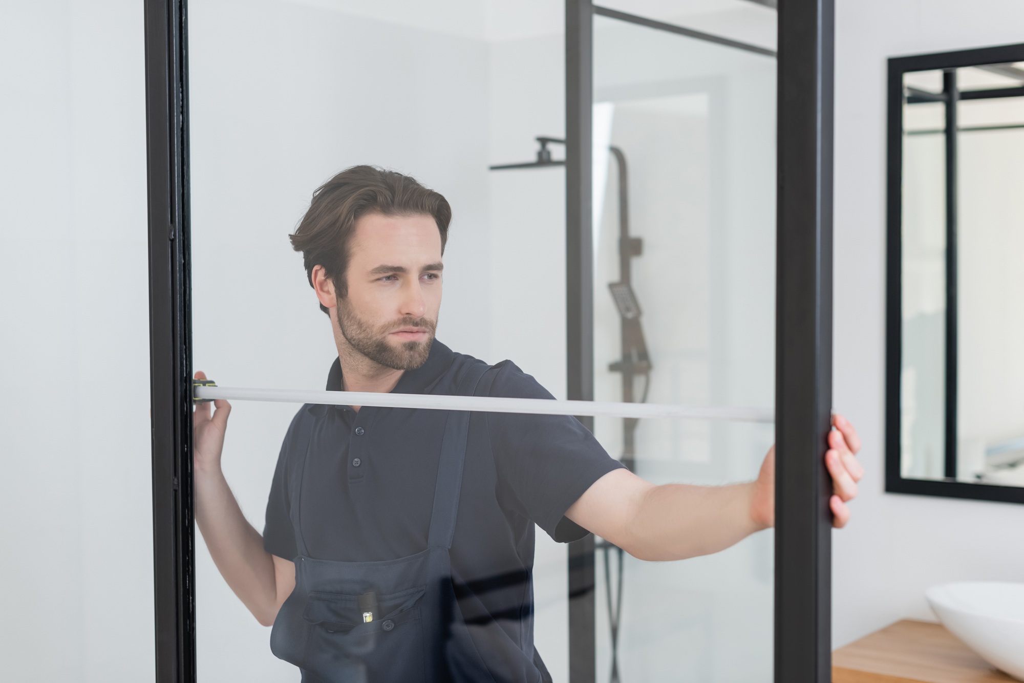 young foreman measuring shower cabin in modern bathroom